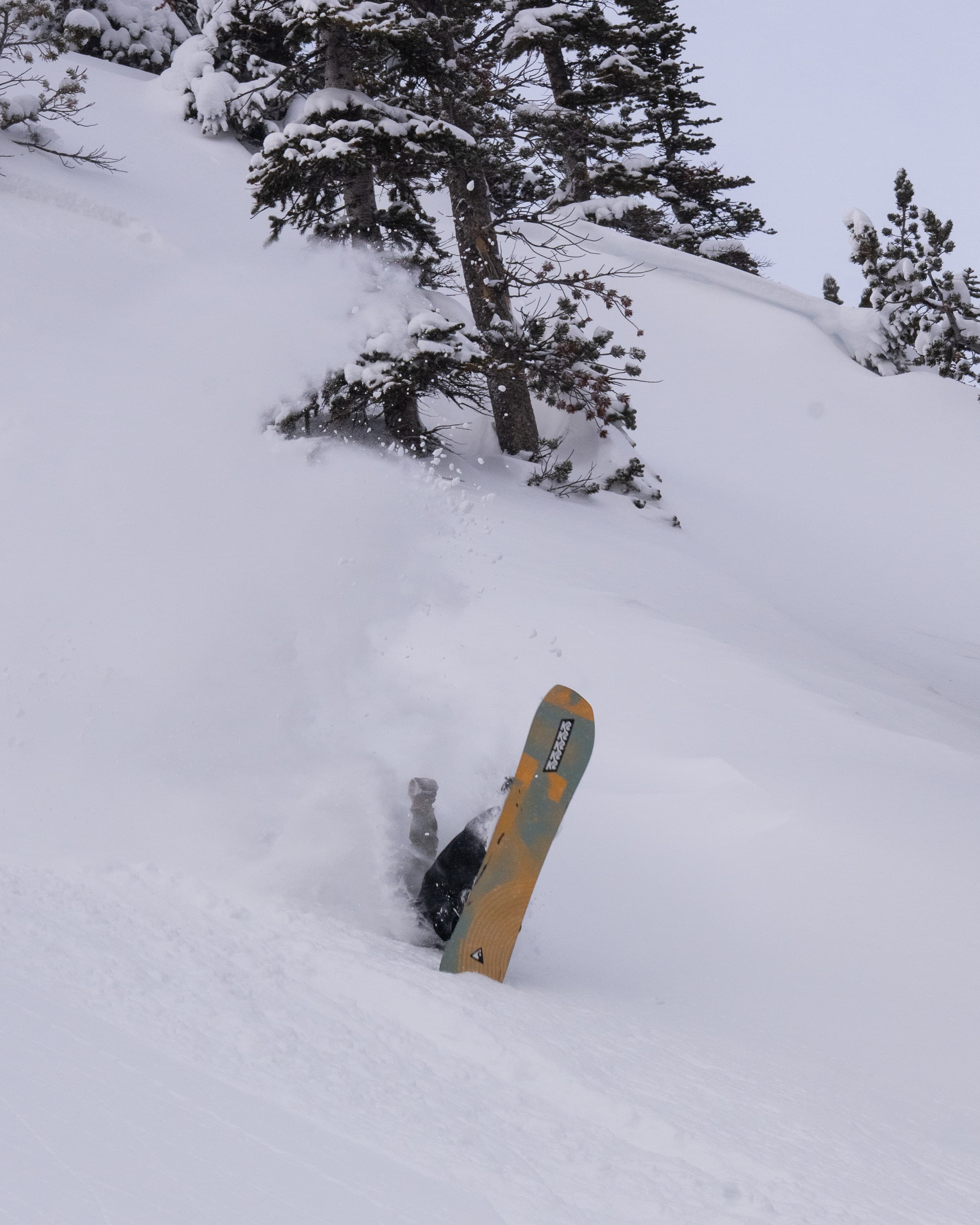 A snowboarder buried in a powder spray with the board sticking up from the snow.