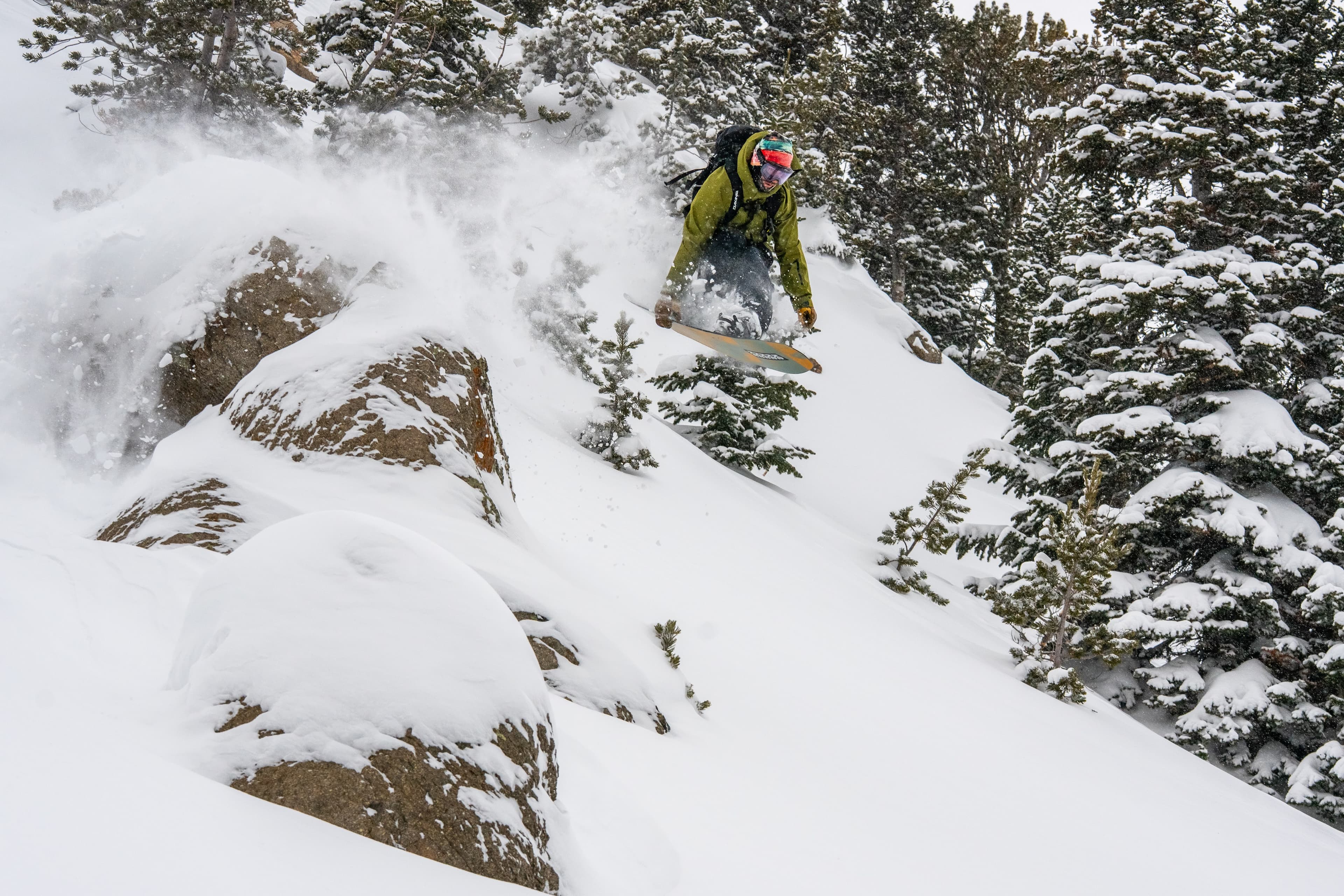 A snowboarder in the air off a snow-covered rock near the Roost.